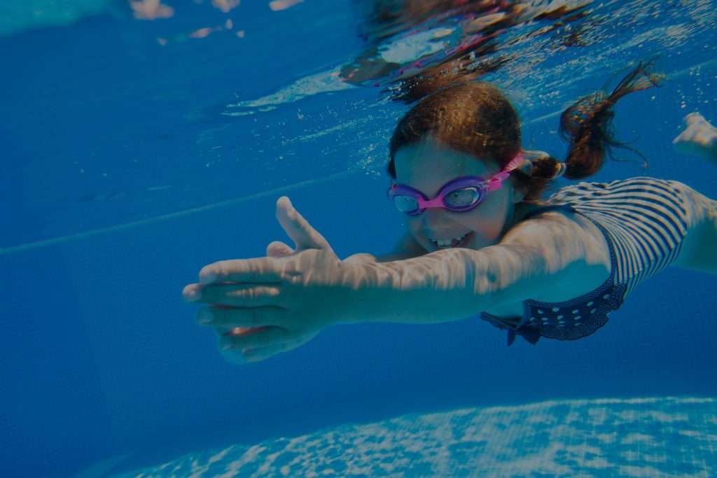 A young girl gracefully swimming underwater in a pool.